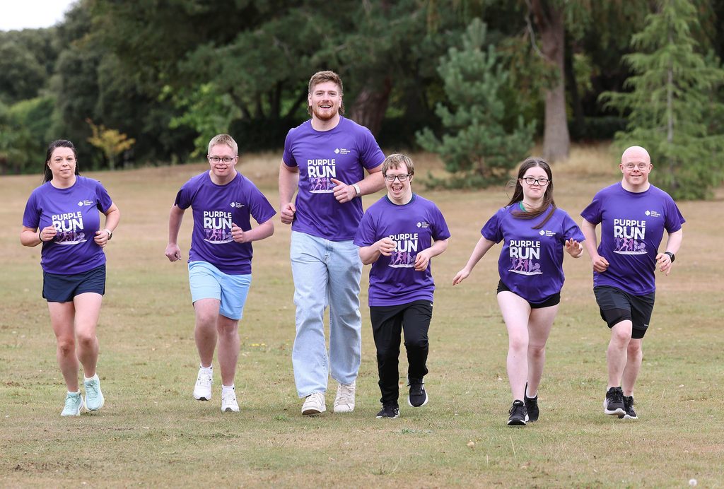 Picture of adults and adults with Down syndrome in a park with Rugby star Joe McCarthy in Purple t-shirts