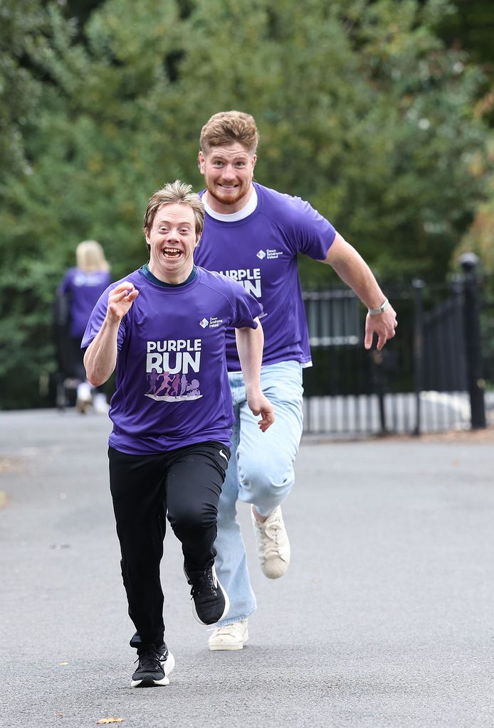 Picture of a man with Down syndrome running in a park with Rugby star Joe McCarthy in Purple t-shirts