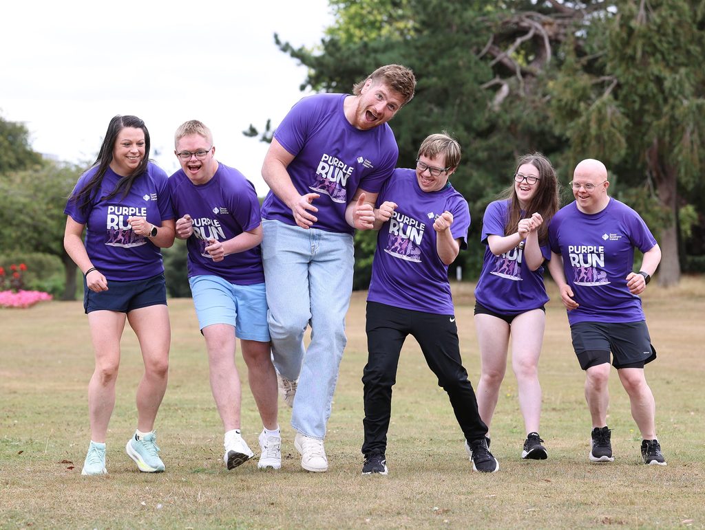 Picture of adults and adults with Down syndrome in a park with Rugby star Joe McCarthy in Purple t-shirts