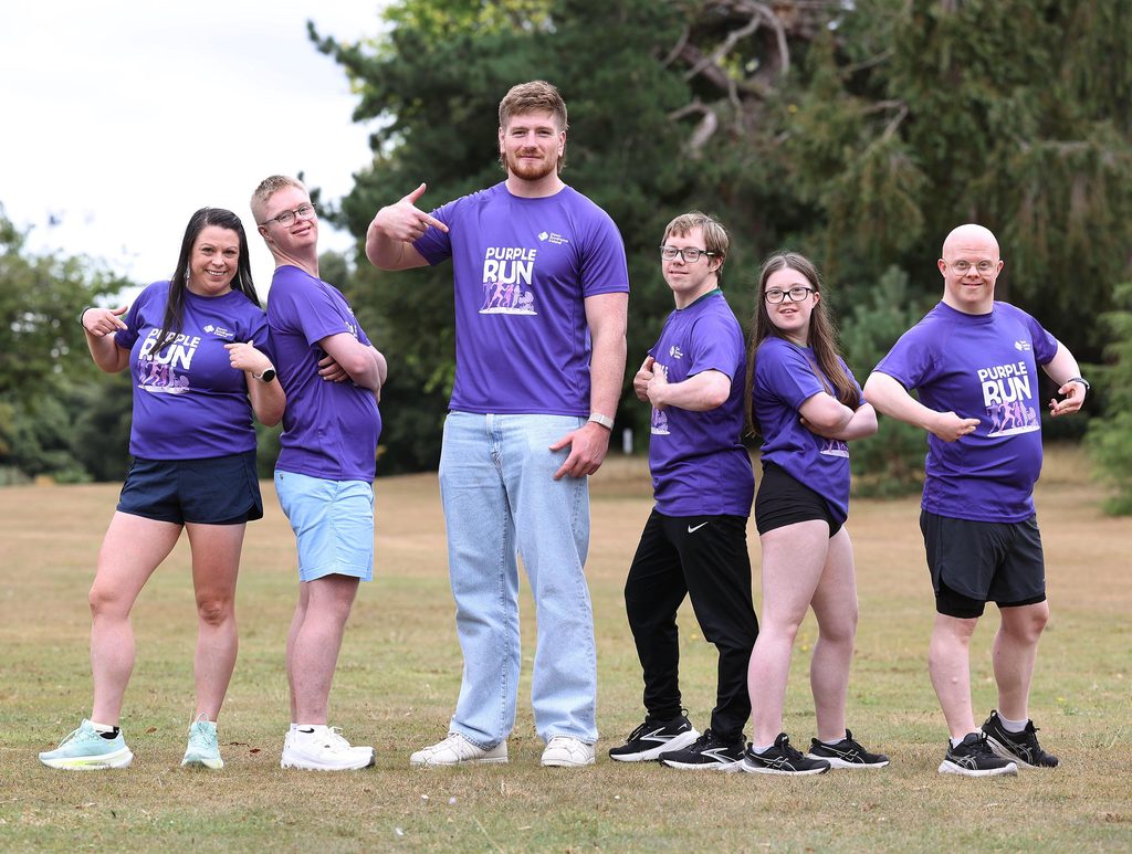 Picture of adults and adults with Down syndrome in a park with Rugby star Joe McCarthy in Purple t-shirts